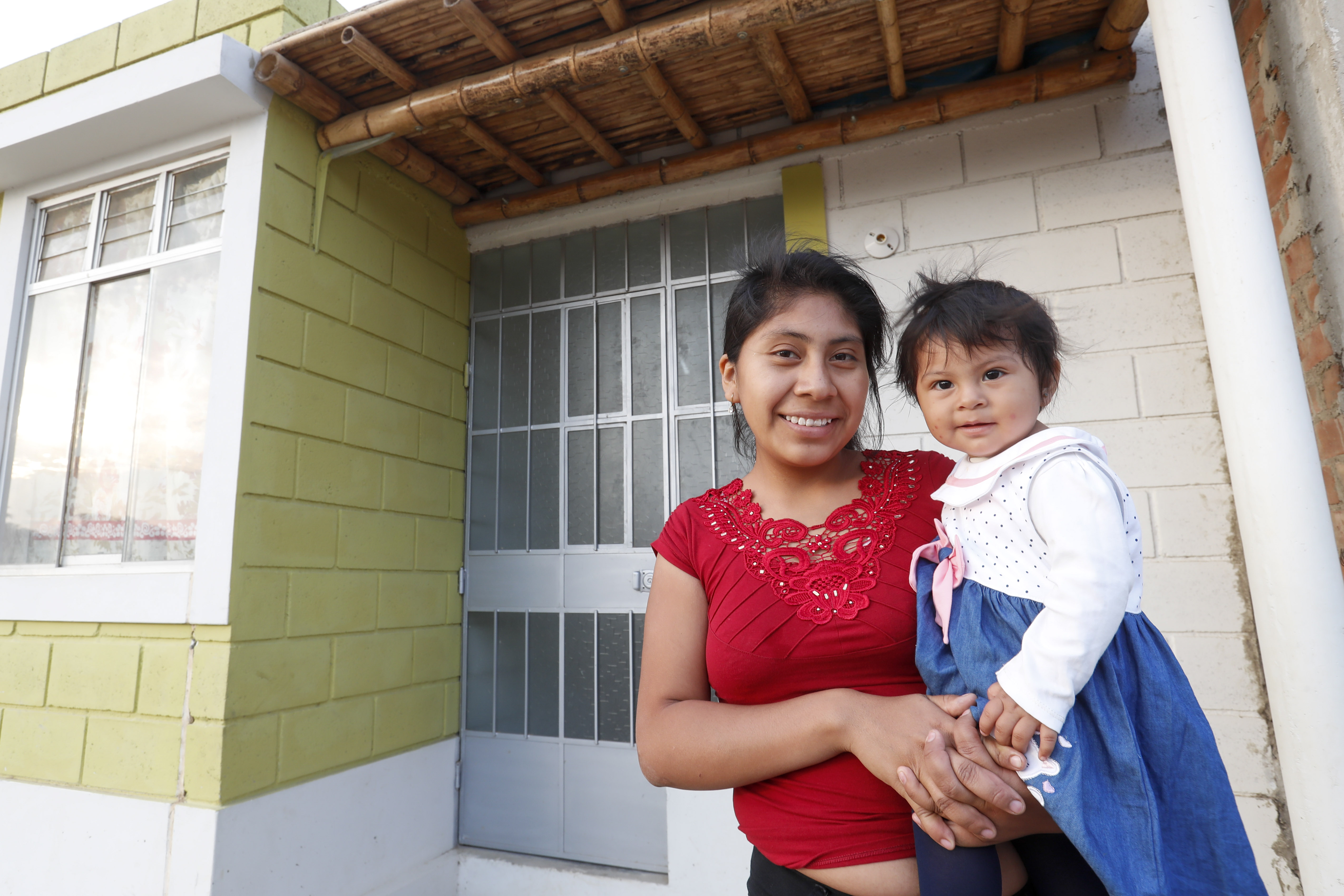 Foto de una madre y su hijo frente a una vivienda.