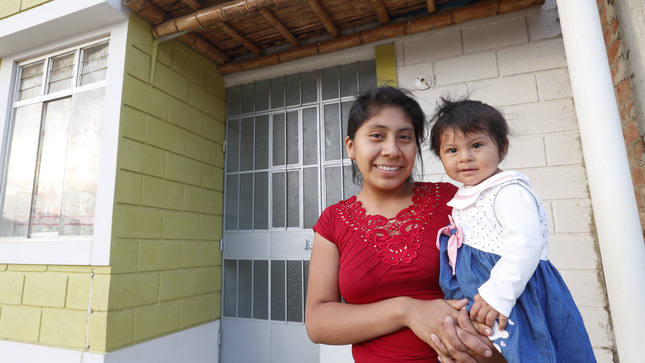 Foto de una madre y su hijo frente a una vivienda.  