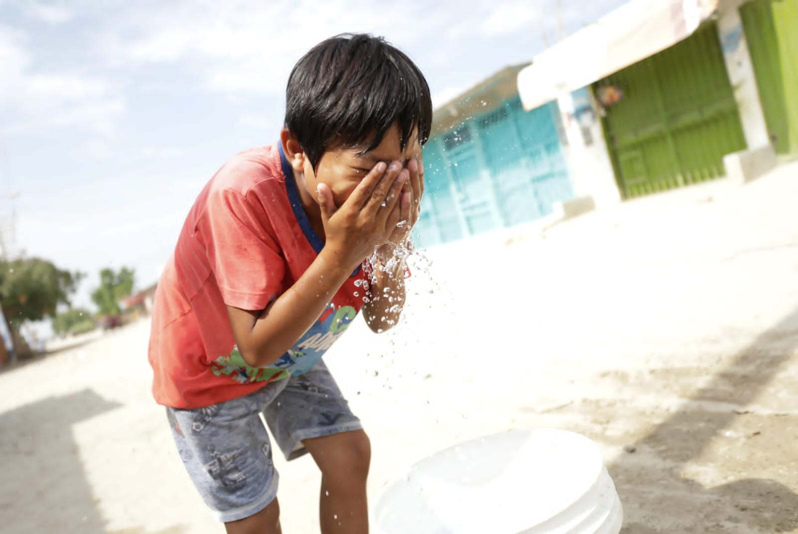 Niño piurano sontiente se moja el rostro con agua de un balde.