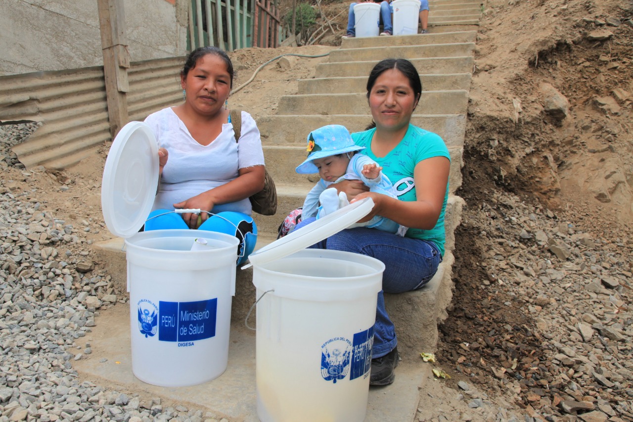 ^Personal de salud enseña a lavar los baldes adecuadamente para depositar el agua.