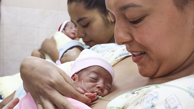 Se ve una mama teniendo a su bebé prematuro en su pecho en contacto piel con piel.