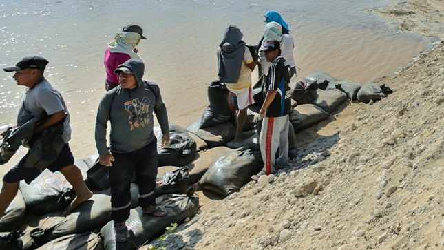 En la foto aparecen ciudadanos al borde del rio colocando bolsas de arena para protegerse de inundaciones