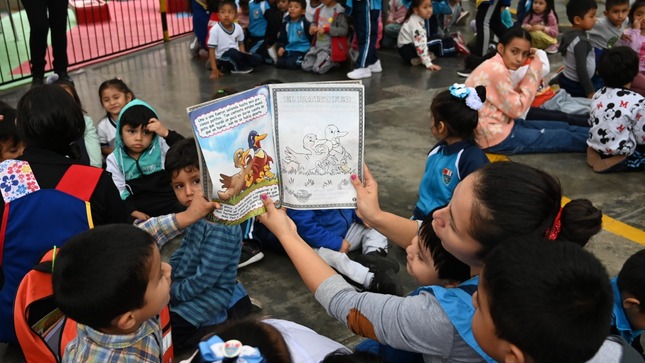 Fotografía de docente junto a los pequeños de inicial, leyéndoles un cuento para calmarlos, tras la ocurrencia de un sismo, durante simulacro.