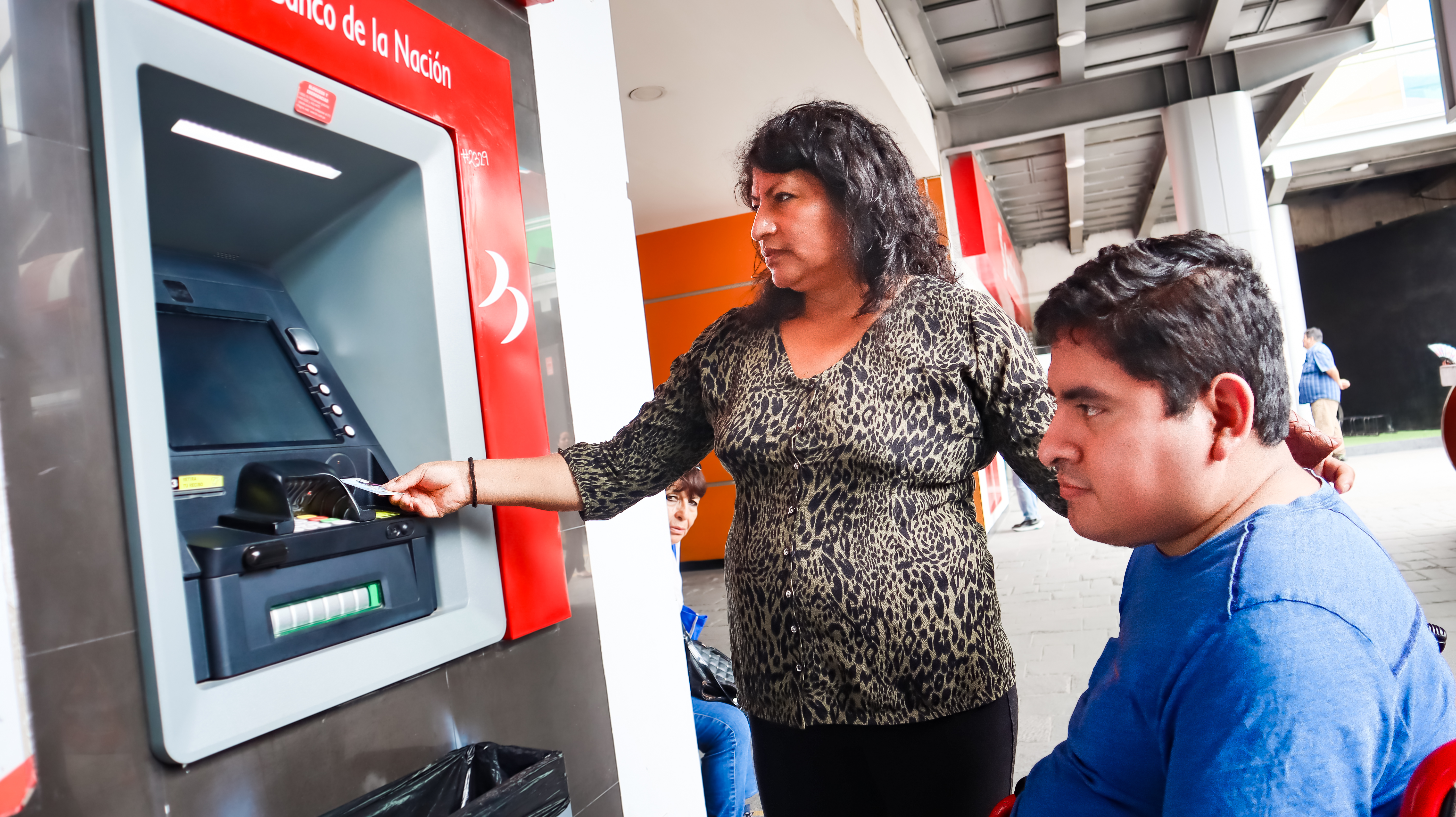 usuario y persona autorizada realizando el cobro de su pensión en el banco