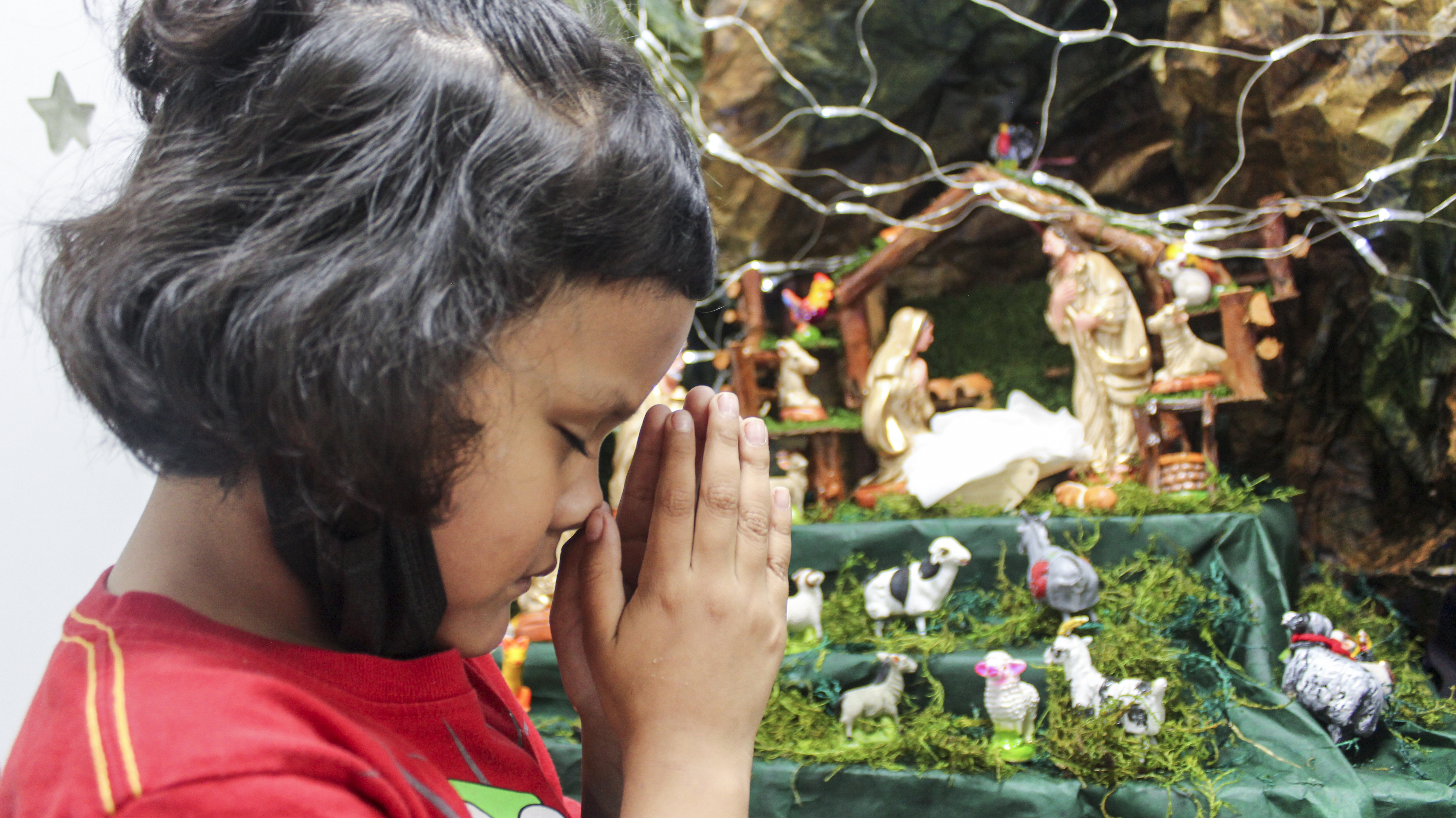 Niña orando frente a nacimiento