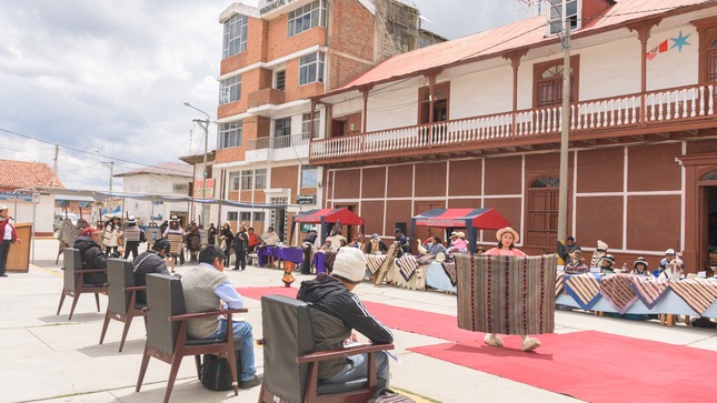 
La imagen muestra el concurso de manta junina con jueces evaluando las creaciones coloridas mientras los participantes esperan con orgullo. La diversidad de colores y diseños resalta la riqueza cultural de la tradición. Una escena vibrante que captura la esencia del evento.