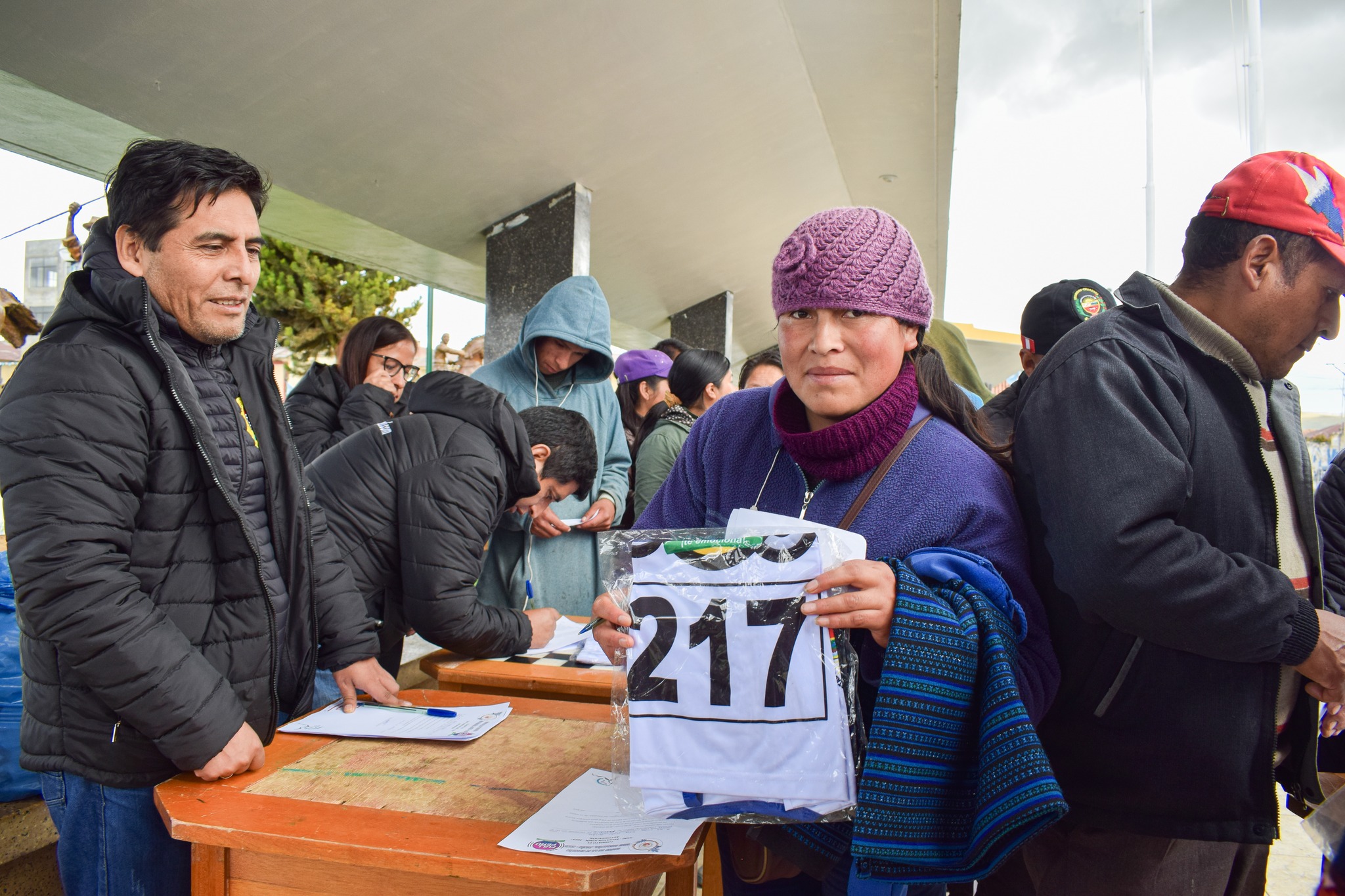 Imagen emocionante: Señora feliz sostiene su camiseta en la entrega para la Mini Maratón Junín 2023, Plaza de Armas llena de diversidad y anticipación