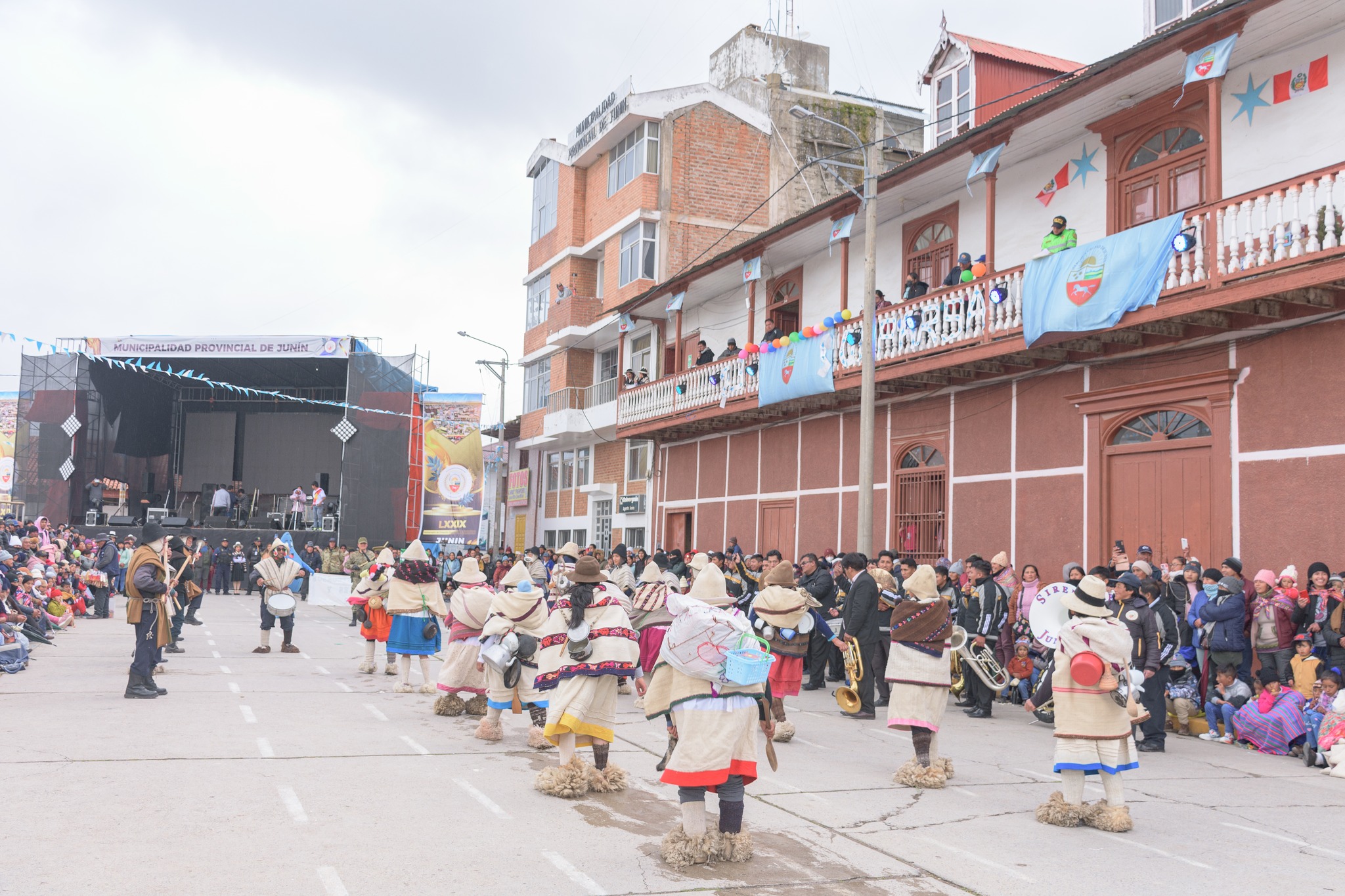 La imagen captura el desfile del 79º aniversario de Junín, con participantes pasando, espectadores animados y un jurado atento. Las expresiones emocionadas de los participantes y la interacción con la audiencia resaltan la celebración vibrante, mientras el jurado evalúa las actuaciones, añadiendo un elemento de competencia y reconocimiento al evento festivo