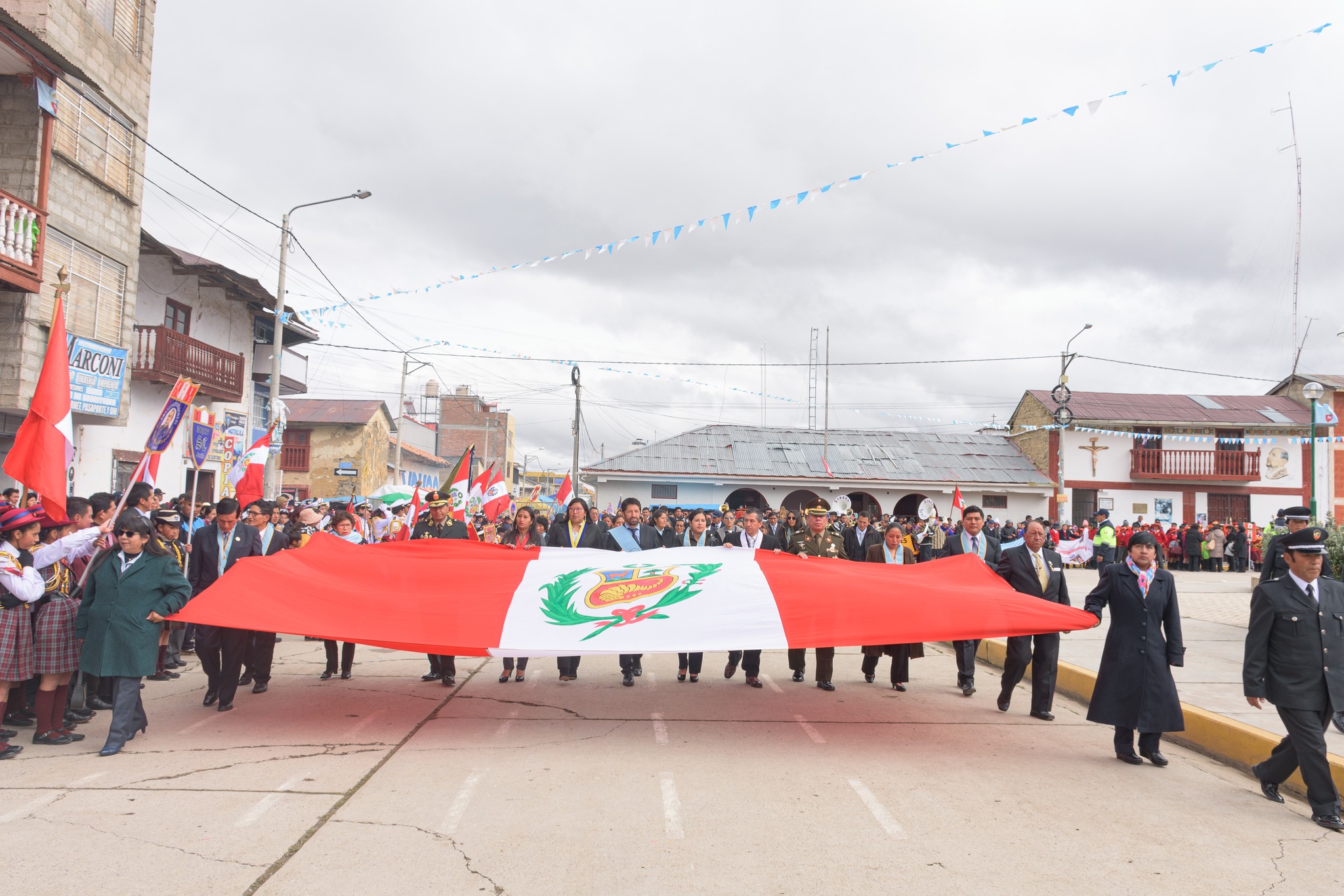 La imagen muestra a las autoridades municipales de pie, con atuendos formales, sosteniendo con orgullo la bandera de Perú. La escena transmite un fuerte sentido de unidad y compromiso patriótico, destacando la solemnidad del momento.