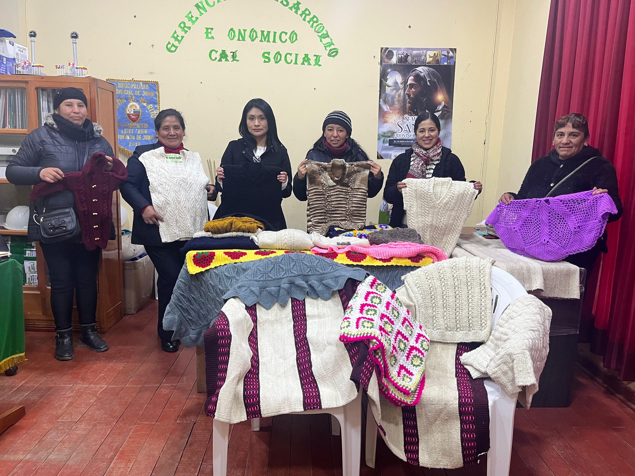 La imagen muestra a las autoridades municipales junto a talentosas madres artesanas, cada una exhibiendo con orgullo sus tejidos a palitos, crochet y telar. La escena destaca la diversidad y calidad de las creaciones, reflejando el espíritu emprendedor y creativo de la comunidad de Junín.