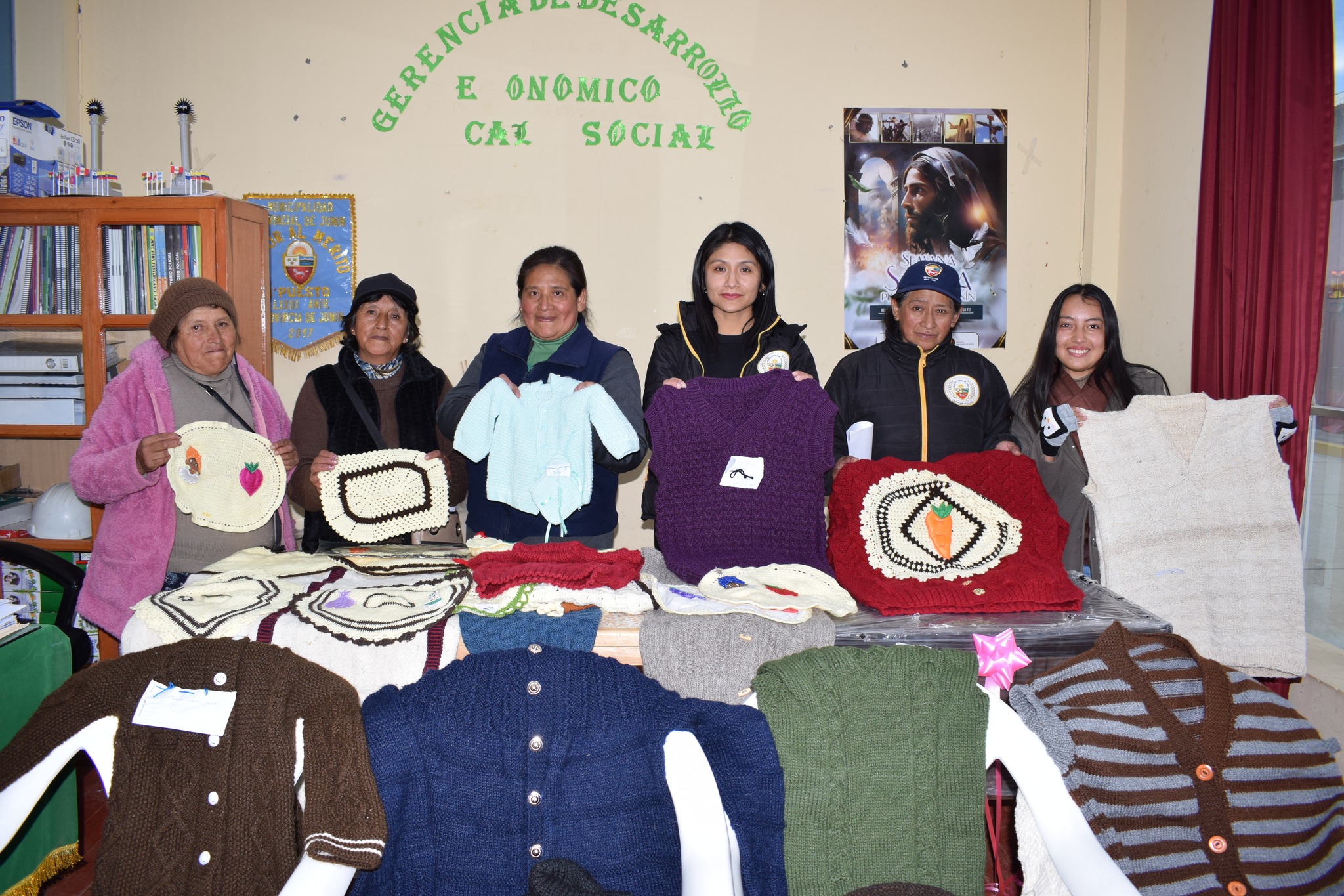 En la imagen, una colorida exhibición de tejidos a crochet y palitos del talentoso equipo del Comedor Popular Nidia Vilchez en Junín adorna el espacio. La Gerenta Judith Chaves Panduro y Susana Chuco Chacchca observan con admiración, mientras la escena refleja un ambiente de camaradería y celebración. La Gerencia de Desarrollo Económico Local y Social respalda este proyecto de micro emprendimiento, resaltando la maestría artesanal, la conexión comunitaria y el apoyo instituciona