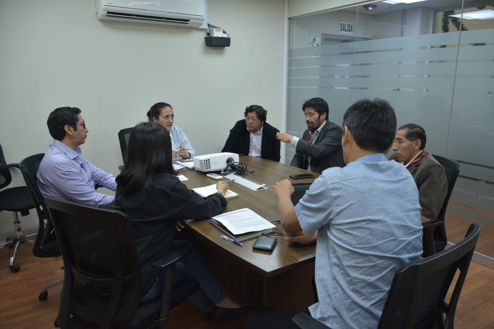 La imagen muestra al Alcalde Elio Zevallos Meza y a Rossana Acuña Delgado liderando una reunión en el Ministerio de Cultura sobre la restauración de Chacamarca. Gabriel Canto, presidente del frente de defensa, también está presente. La escena refleja colaboración y compromiso en un ambiente de trabajo enfocado.