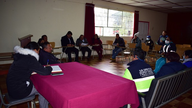 La imagen muestra a Condor Surichaqui liderando una reunión en el Centro de Salud Junín, con autoridades clave discutiendo estrategias para prevenir el fenómeno del Niño. El ambiente refleja cooperación y compromiso, capturando un momento crucial de planificación para garantizar la seguridad ante posibles eventualidades.