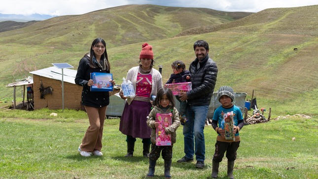 La imagen muestra al alcalde de Junín y la psicóloga junto a una familia, todos sonriendo y sosteniendo juguetes donados en el marco del proyecto "Una Sonrisa por Navidad". La escena transmite la alegría y solidaridad de la iniciativa.