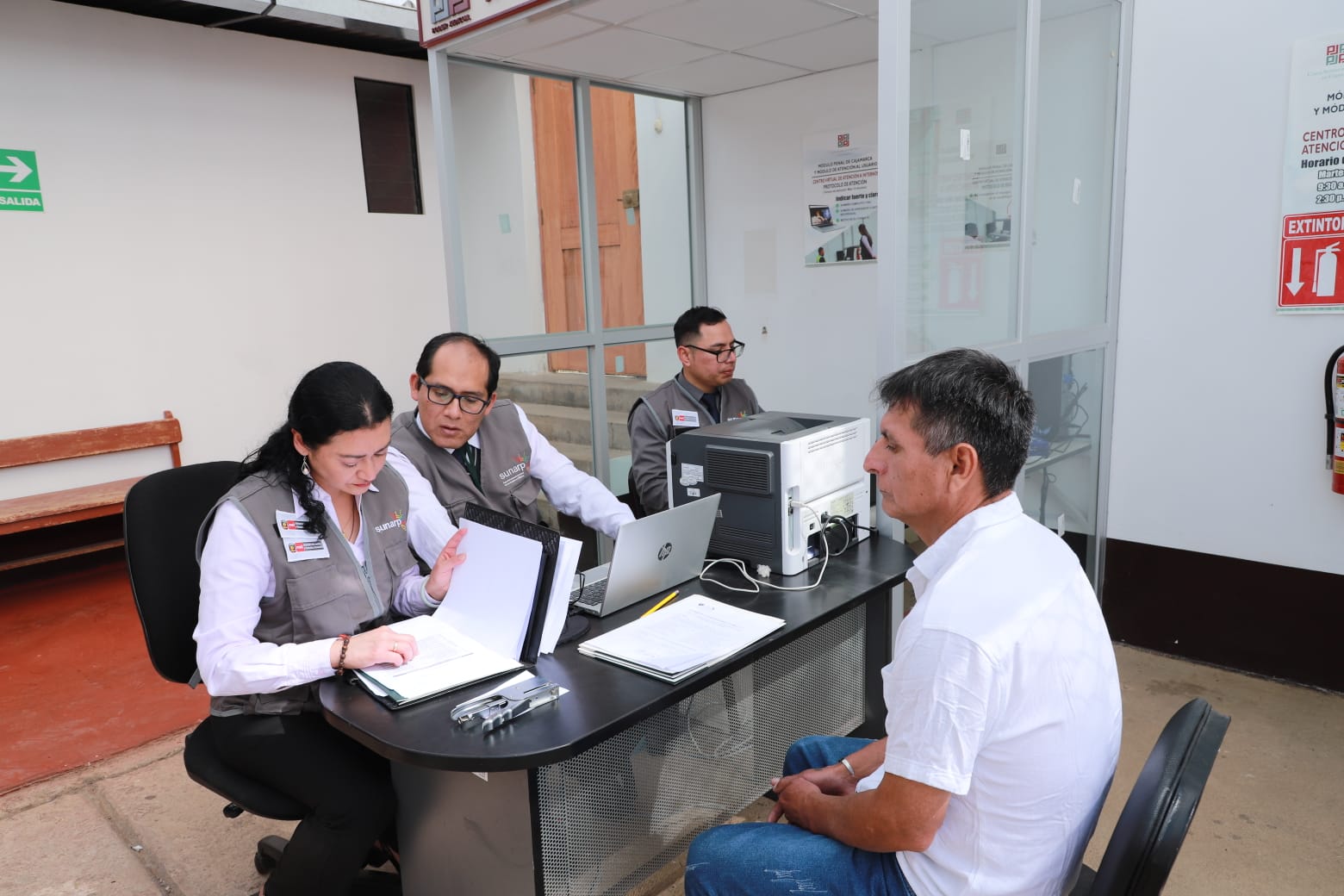 Foto de Servidores de Sunarp sentados al lado de escritorio atienden a internos del penal de Huacariz en Cajamarca