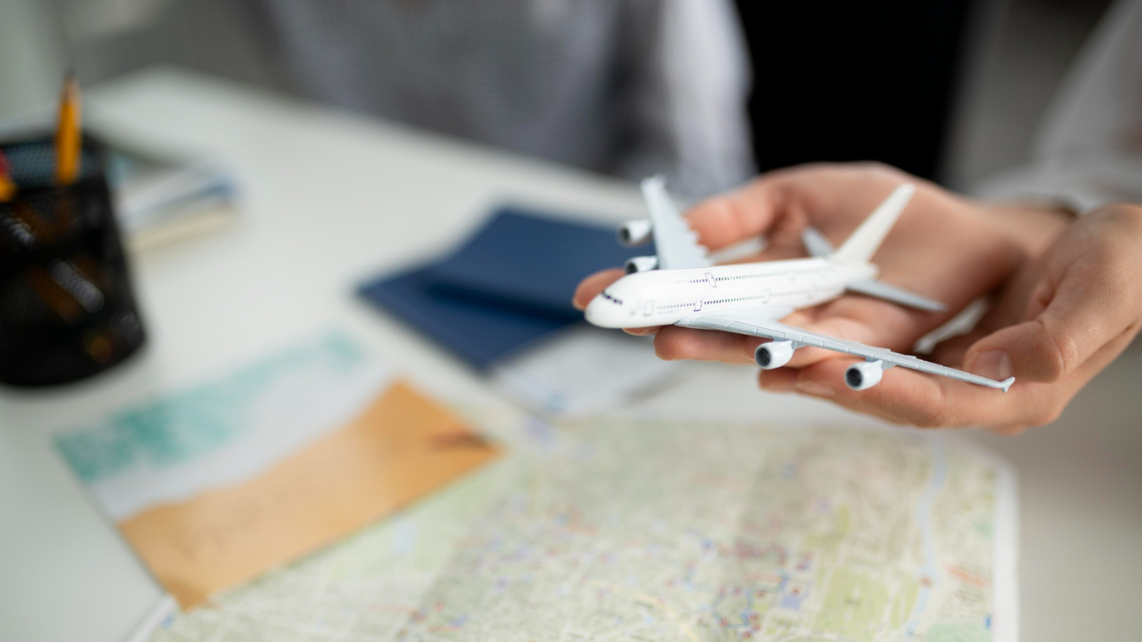 Imagen de la maqueta de un avión sostenida en las palmas de la mano de alguien, con un mapa impreso en la mesa.