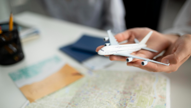 Imagen de la maqueta de un avión sostenida en las palmas de la mano de alguien, con un mapa impreso en la mesa.