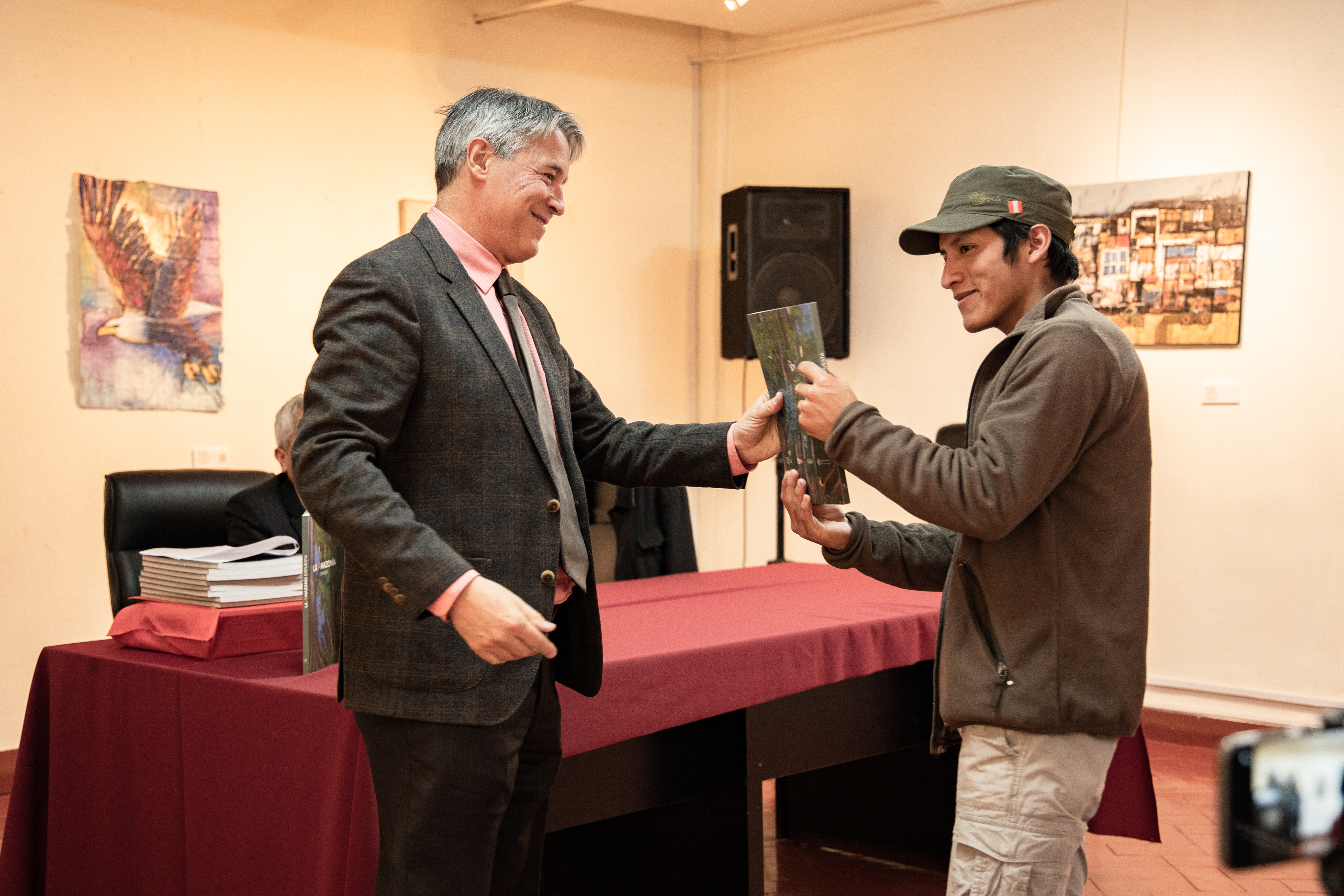 Ministro consejero Pedro Pablo Delgado Hinostroza haciendo entrega del ejemplar del catálogo a un estudiante.