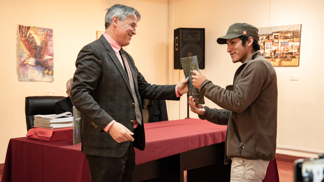 Ministro consejero Pedro Pablo Delgado Hinostroza haciendo entrega del ejemplar del catálogo a un estudiante. 
