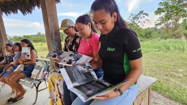 Foto de Mujeres de la localidad de San Lorenzo están sentadas leyendo folletos sobre trámites de la Sunarp