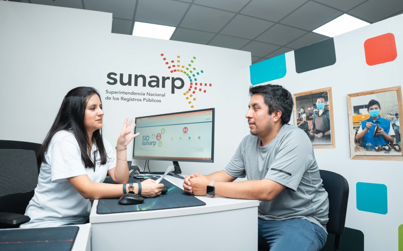 Foto de Servidora de la Sunarp dando información a una persona en una oficina