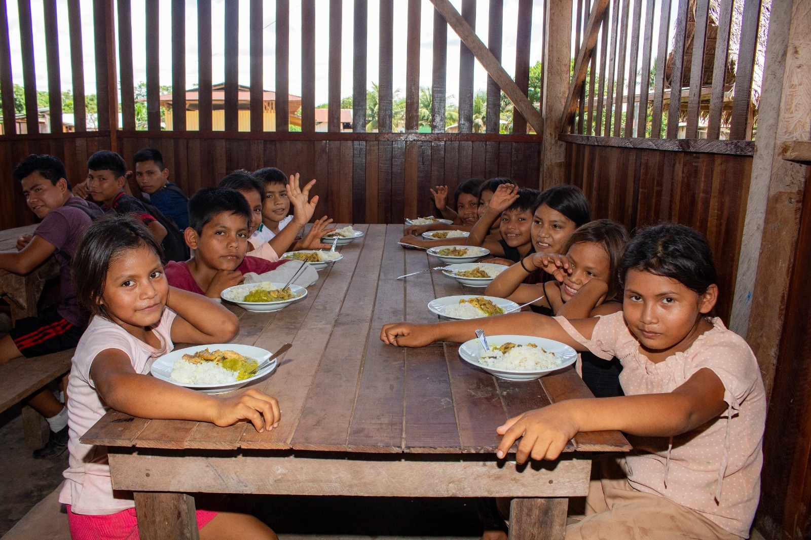 Niños consumen alimento sentados en mesa.