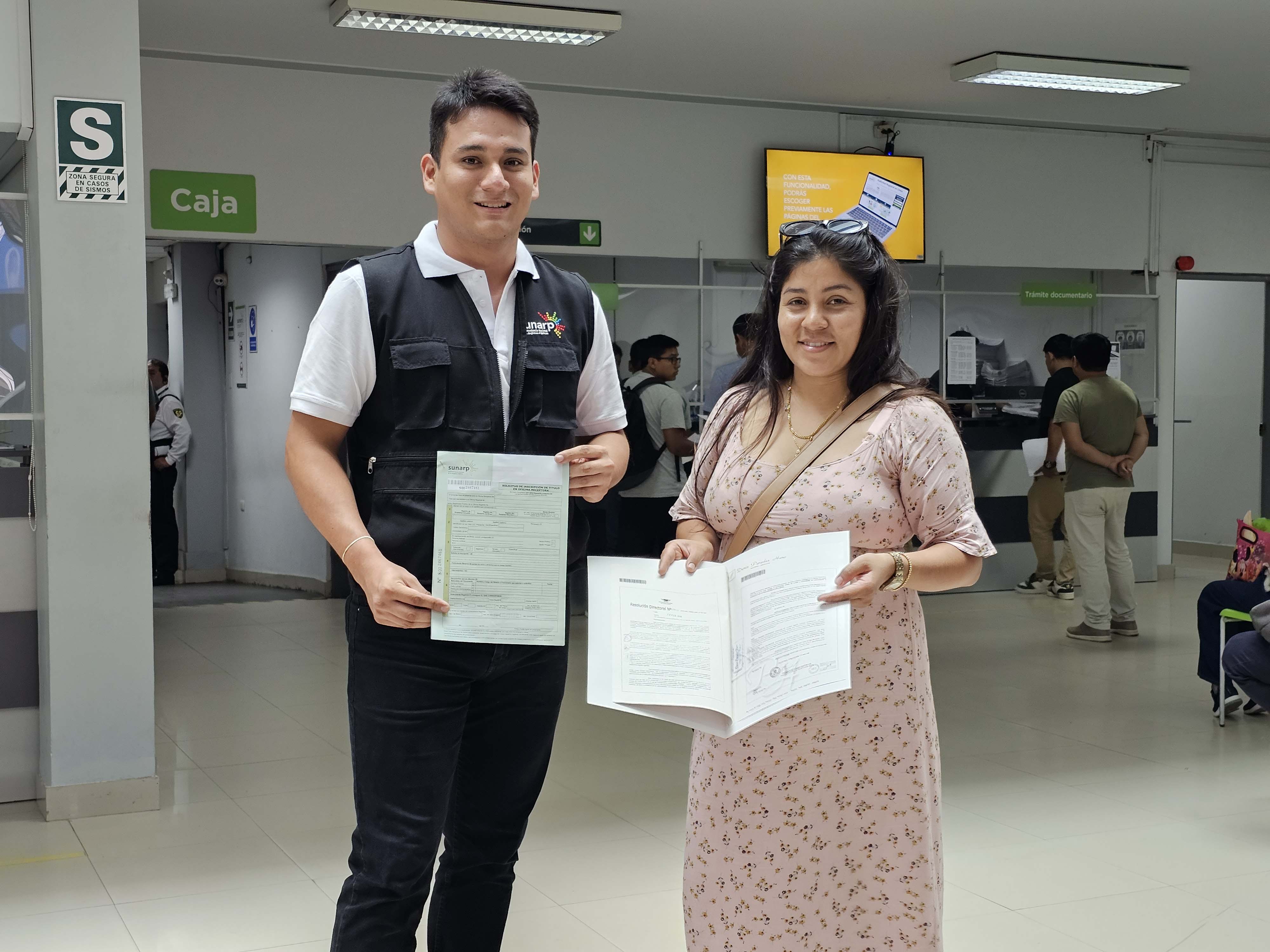 Foto de colaborador de Sunarp y mujer parados dentro de oficina de Sunarp muestran documentos registrales