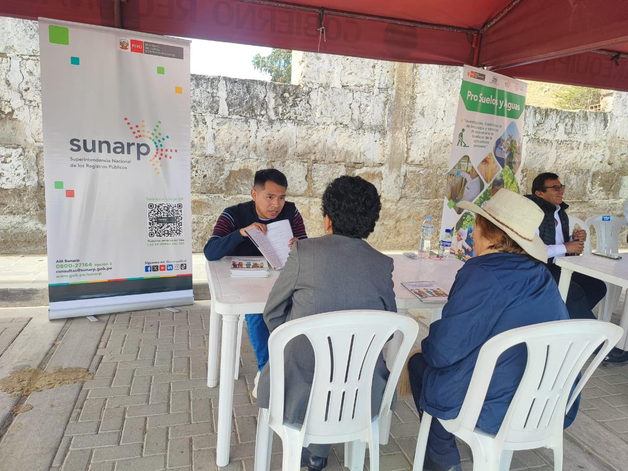 Foto de Un trabajador de Sunarp brinda información a una pareja de adultos mayores en módulo de atención