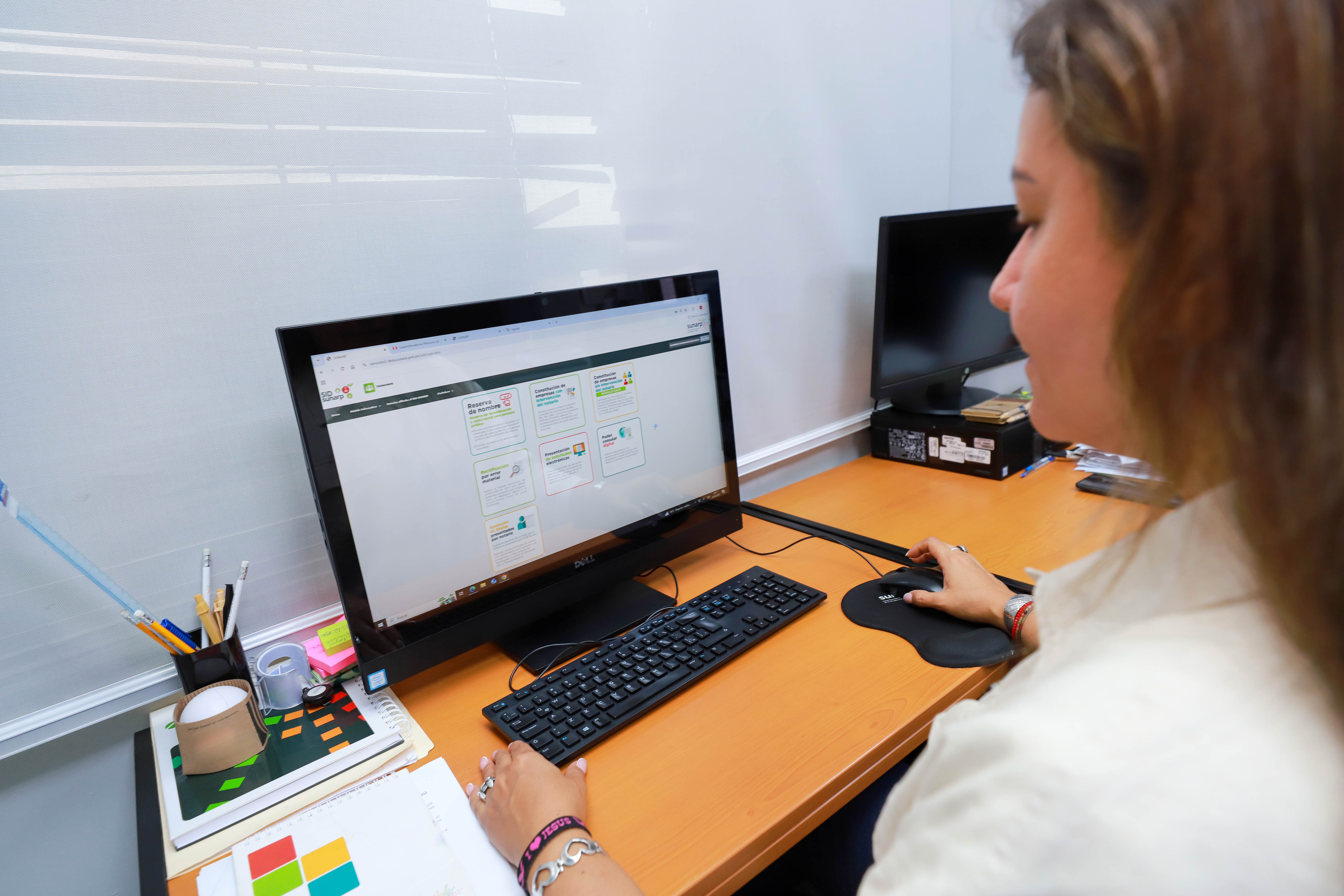 Foto de Trabajadora de Sunarp sentada frente a monitor de pantalla de una PC