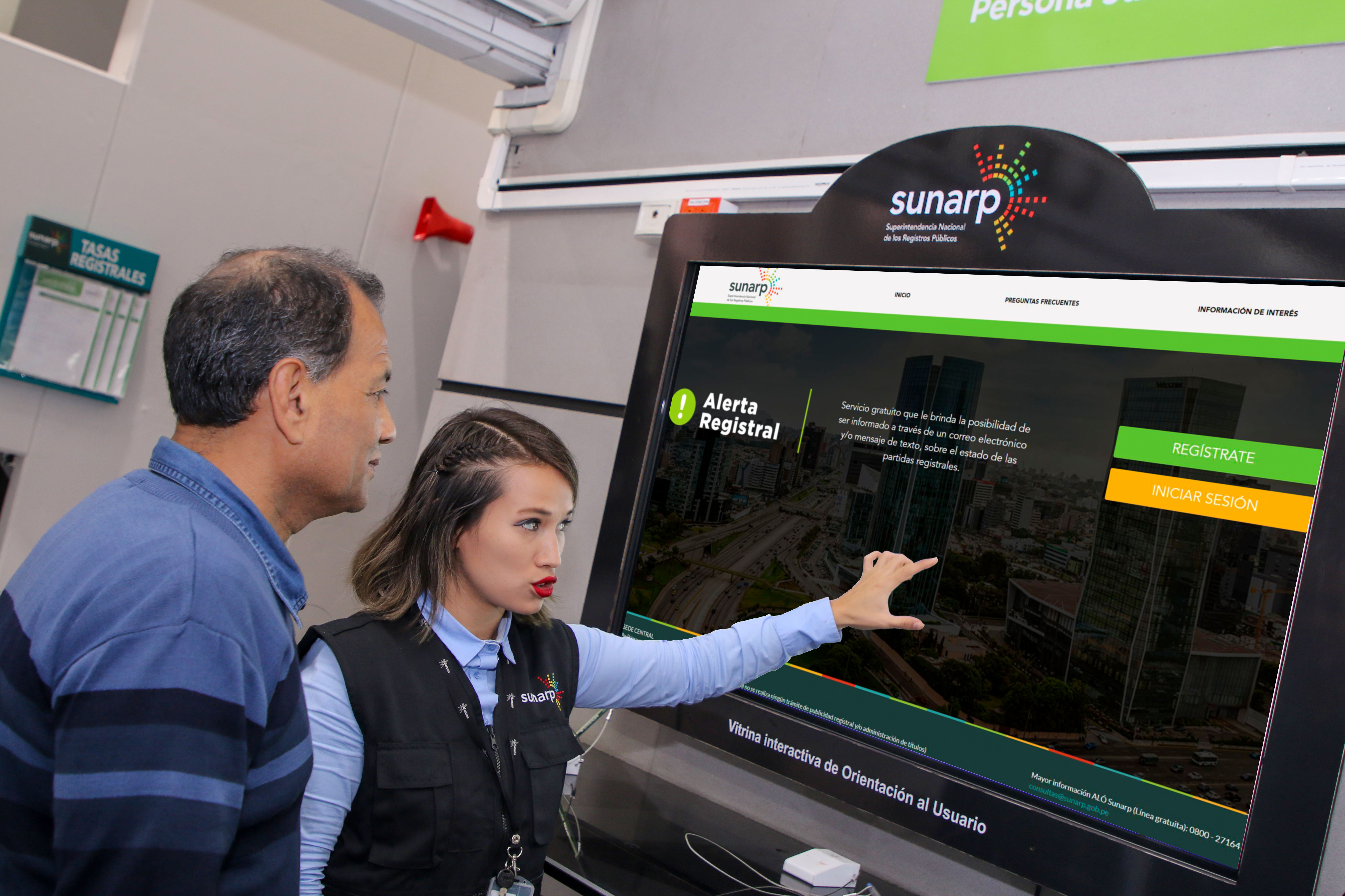 Foto de Servidora de Sunarp muestra información a un hombre en una pantalla