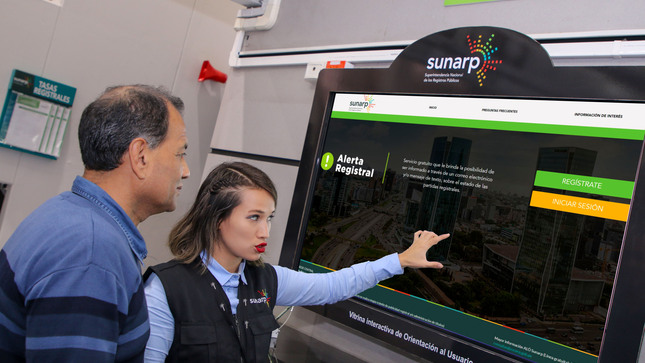 Foto de Servidora de Sunarp muestra información a un hombre en una pantalla