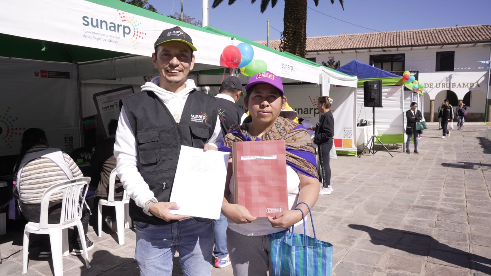 Foto de Trabajador de Sunarp y poblador de Cusco posan para la foto mostrando documentos registrales